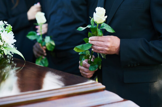 Costo-funerale-5-consigli-per-gestire-al-meglio-la-spesa particolare di persona a lutto che tiene in mano una rosa bianca durante un funerale