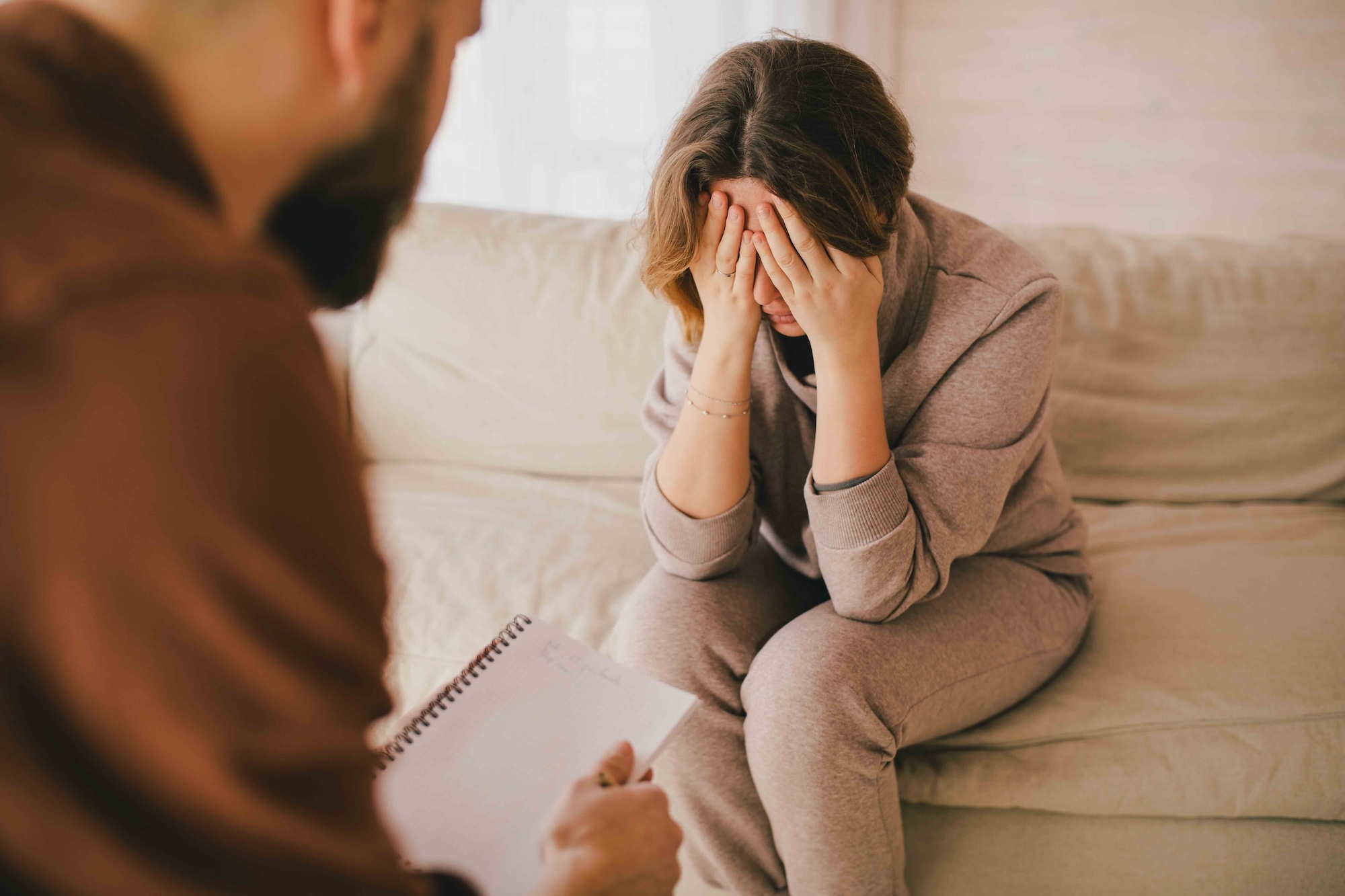 estumulazione-sostegno-psicologico donna addolorata seduta sul divano durante una seduta di psicoterapia, con psicoterapeuta uomo visto di spalle