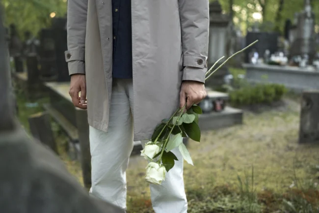 man-visiting-cemetery-with-white-roses uomo al cimitero con due rose bianche davanti alla tomba di un caro